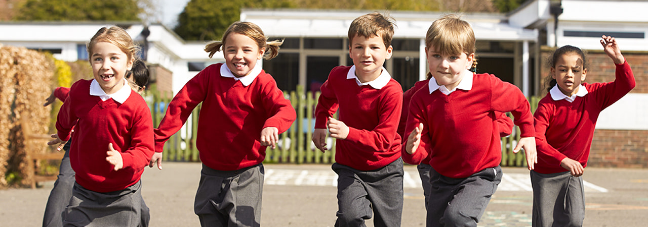 Group of schoolchildren in red uniforms running and laughing in a playground